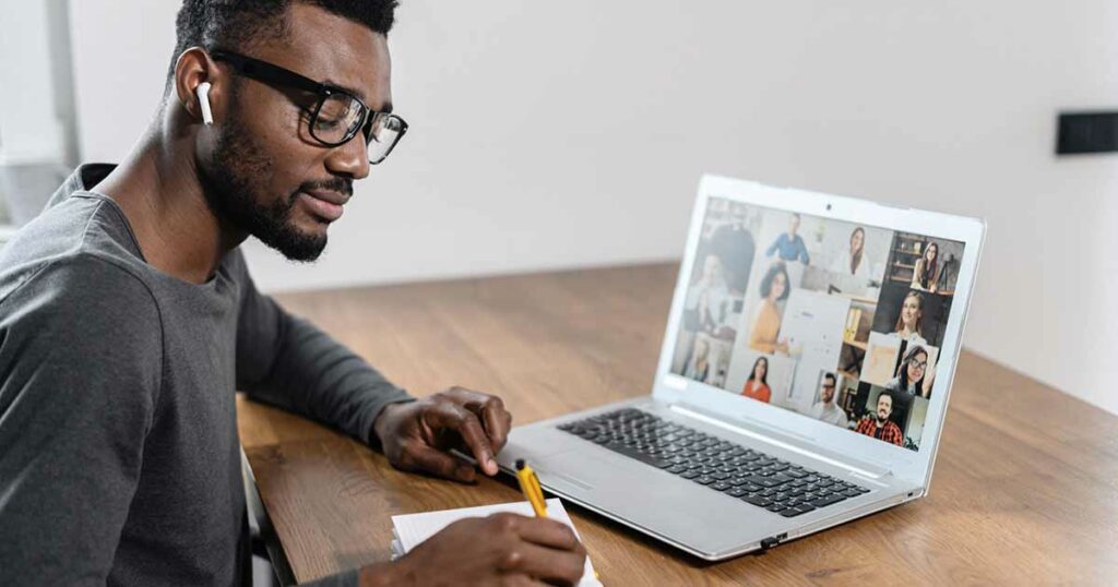 Man attending a meeting online and writing notes in a notepad.