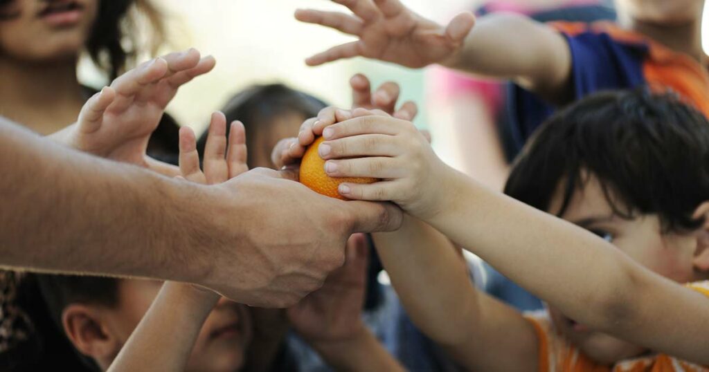 Lots of hands of various tween ages reaching for a piece of fruit being offered by an adult hand.