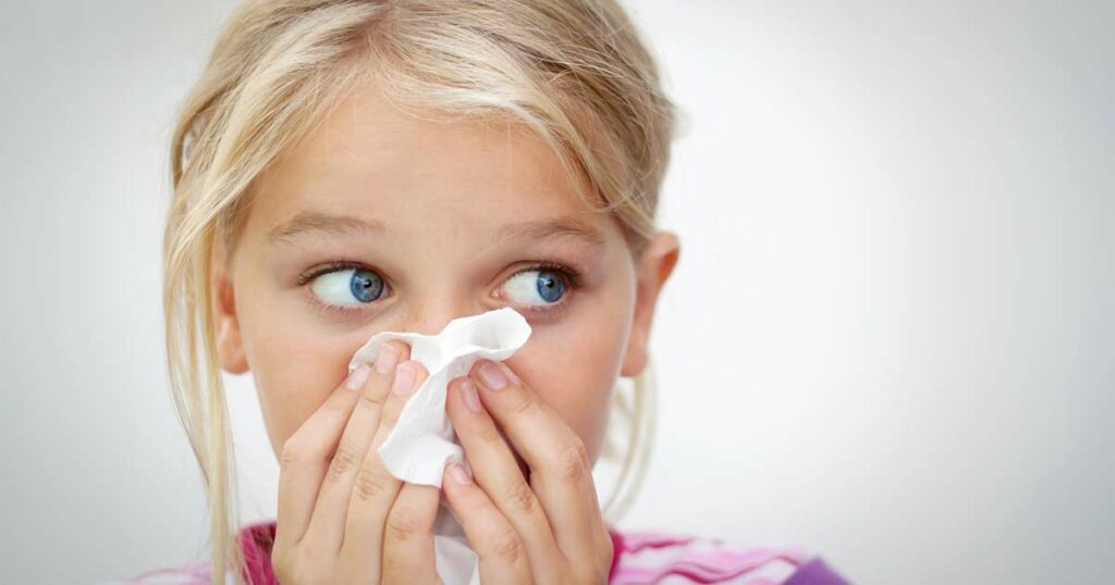 Young girls holding tissue to her  nose because of stuffed nasal passages.