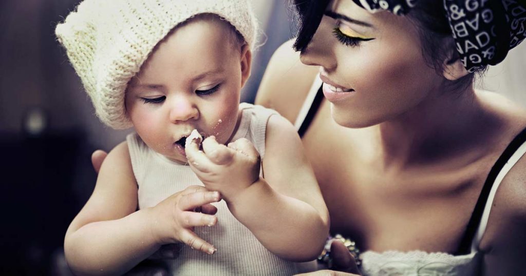 Mother holding her infant while the baby eats a piece of bread with their hand