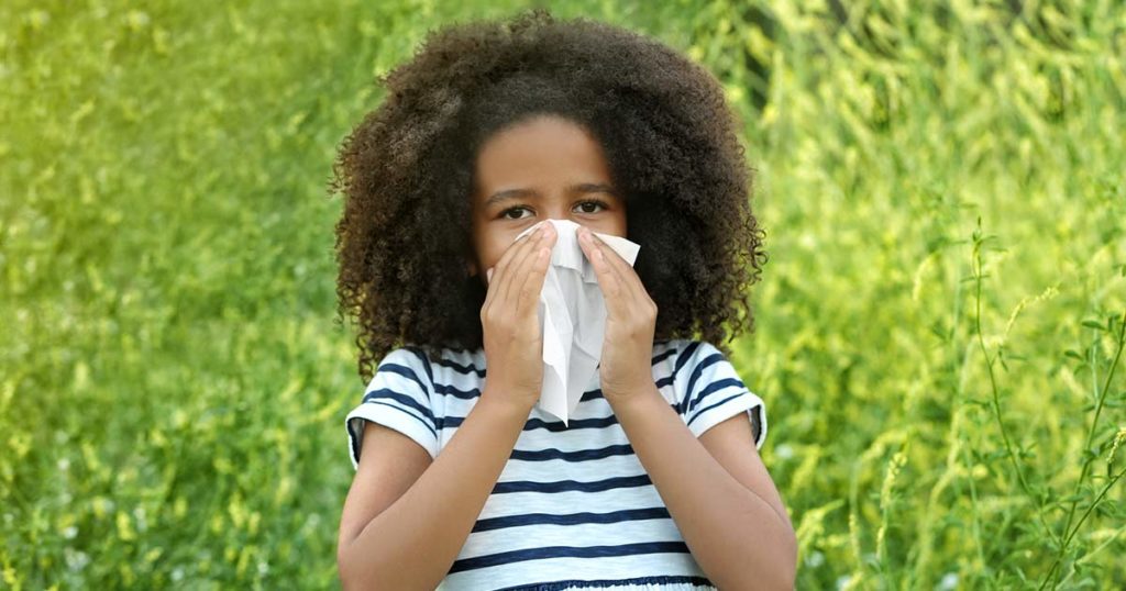 Photo of Black tween girl holding a tissue to her nose for spring allergies. She