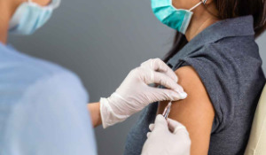 Thumbnail photo of person in surgical gloves giving woman a Covid-19 vaccine in her arm.