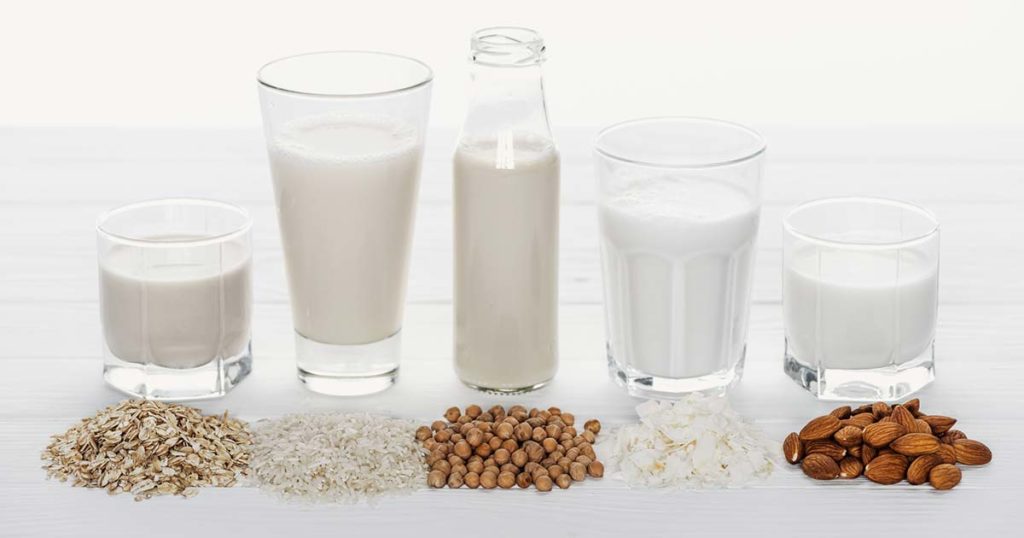 5 different types of vegan milk with their source under the milk: coconut, chickpea, almond, cashew, and hemp.